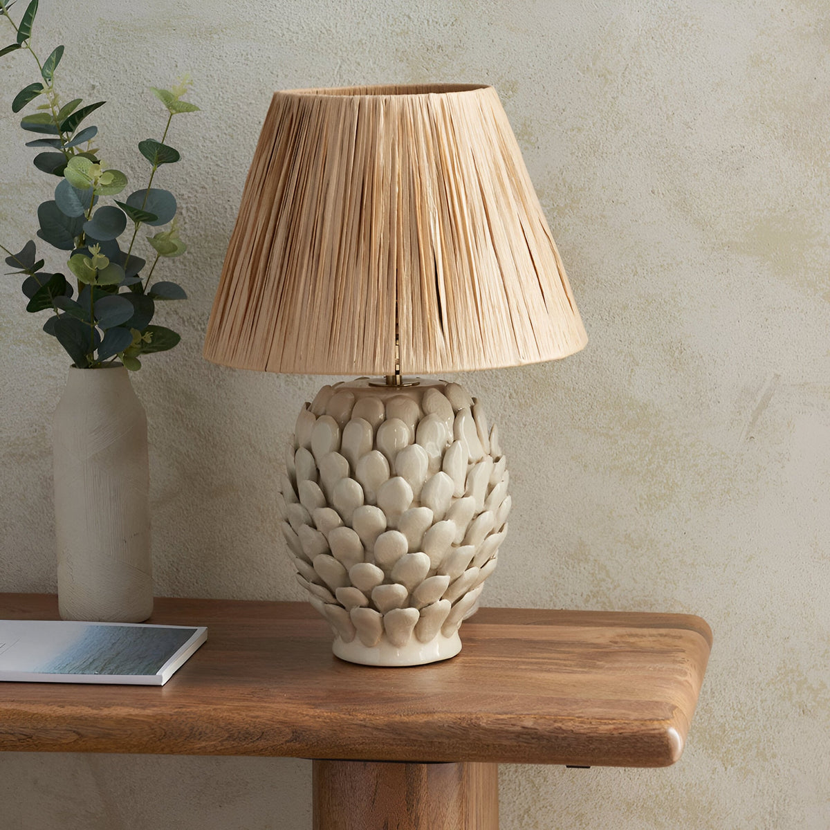 Endon Caldford ceramic table lamp with ivory crackle-glazed leaf-textured base and tapered natural raffia shade, styled on a wood console with eucalyptus.