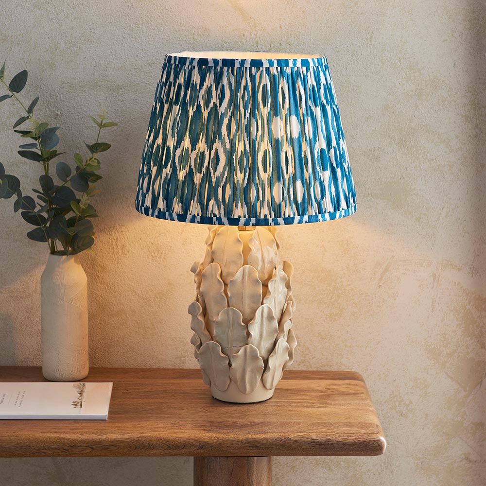 Endon Caldford Ikat 35cm table lamp with ivory crackle-glaze ceramic leaf base and pleated blue Ikat shade, styled on a wooden console beside eucalyptus.