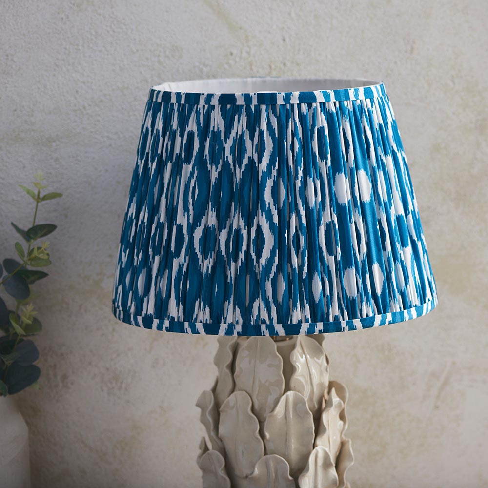 Endon Caldford Ikat 35cm table lamp with a pleated blue and cream Ikat shade on an ivory ceramic leaf-sculpted base against a pale wall.