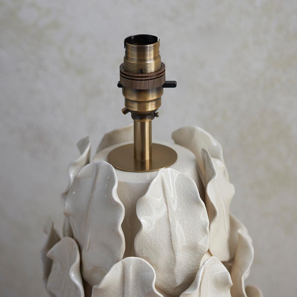 Close-up of the Endon Caldford table lamp showing its brushed aged brass B22 lamp holder above the ivory crackle-glaze ceramic leaf base.