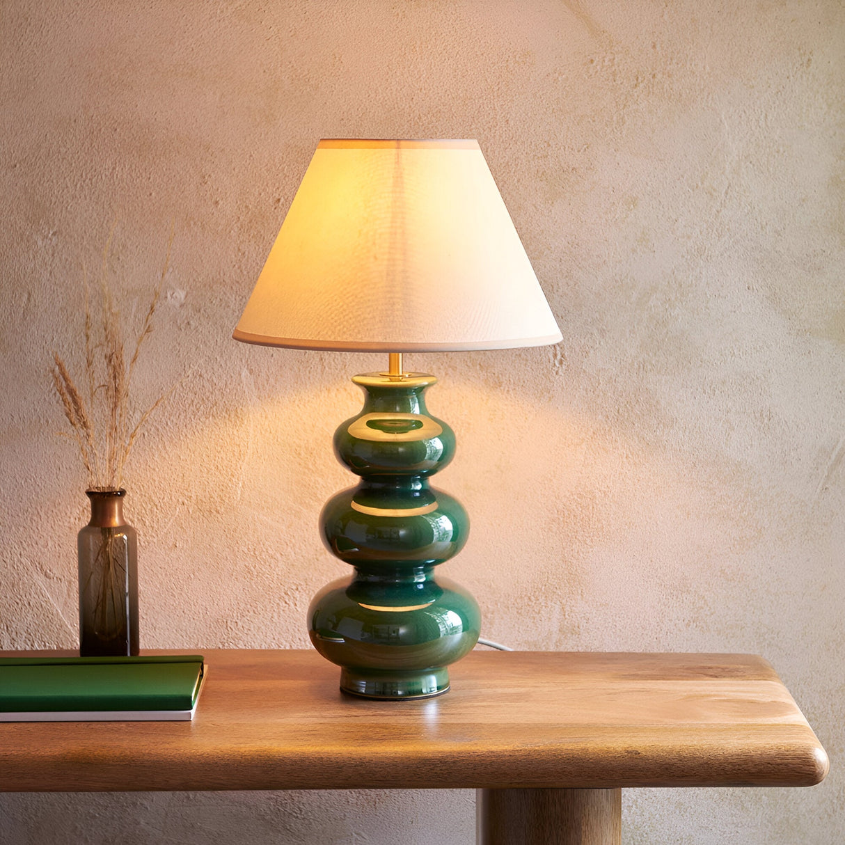 Carlstead Ivy Table Lamp in glossy green ceramic with a tiered gourd-shaped base and white fabric shade, shown lit on a wooden console table.