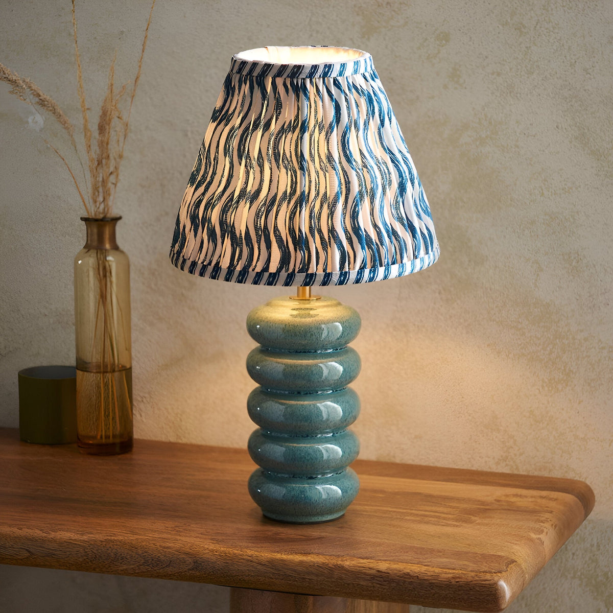 Cliffstead Table Lamp with stacked blue ceramic base and brass fitting, topped with a pleated blue and white patterned fabric shade, shown on a wooden table.