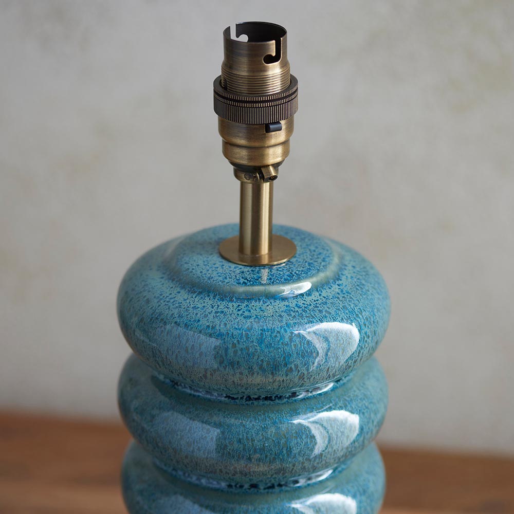 Cliffstead Table Lamp base close-up showing a stacked, curved ceramic body in teal reactive glaze with an aged brass switched B22 lamp holder.