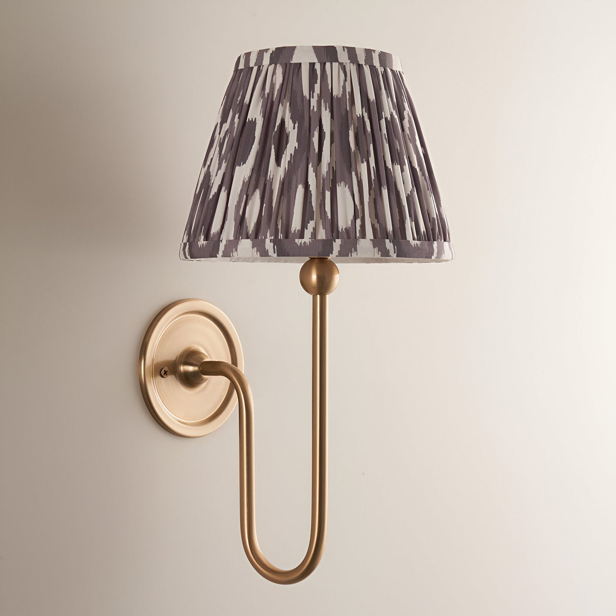 Cliffleigh Ikat Wall Light in antique brass with a pleated grey and white patterned tapered fabric shade, on a plain light background.