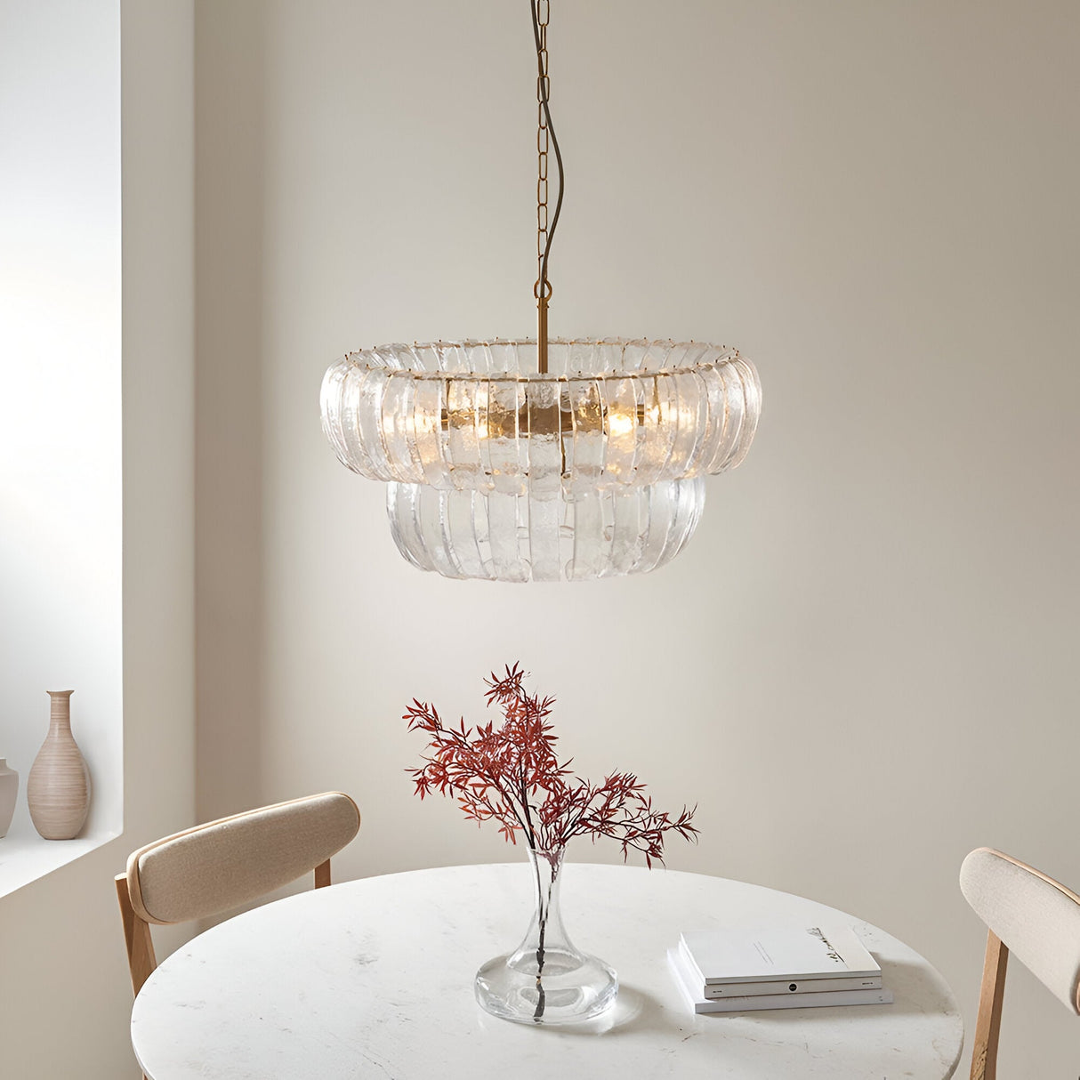 Carlwell 6 Light Pendant in brass, two-tier curved glass design hanging above a round marble dining table in a neutral-toned room.