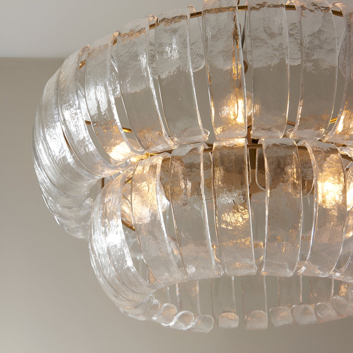 Carlwell 6 Light Pendant in brass, close-up of two-tier curved clear glass panels with illuminated bulbs and brushed brass frame.