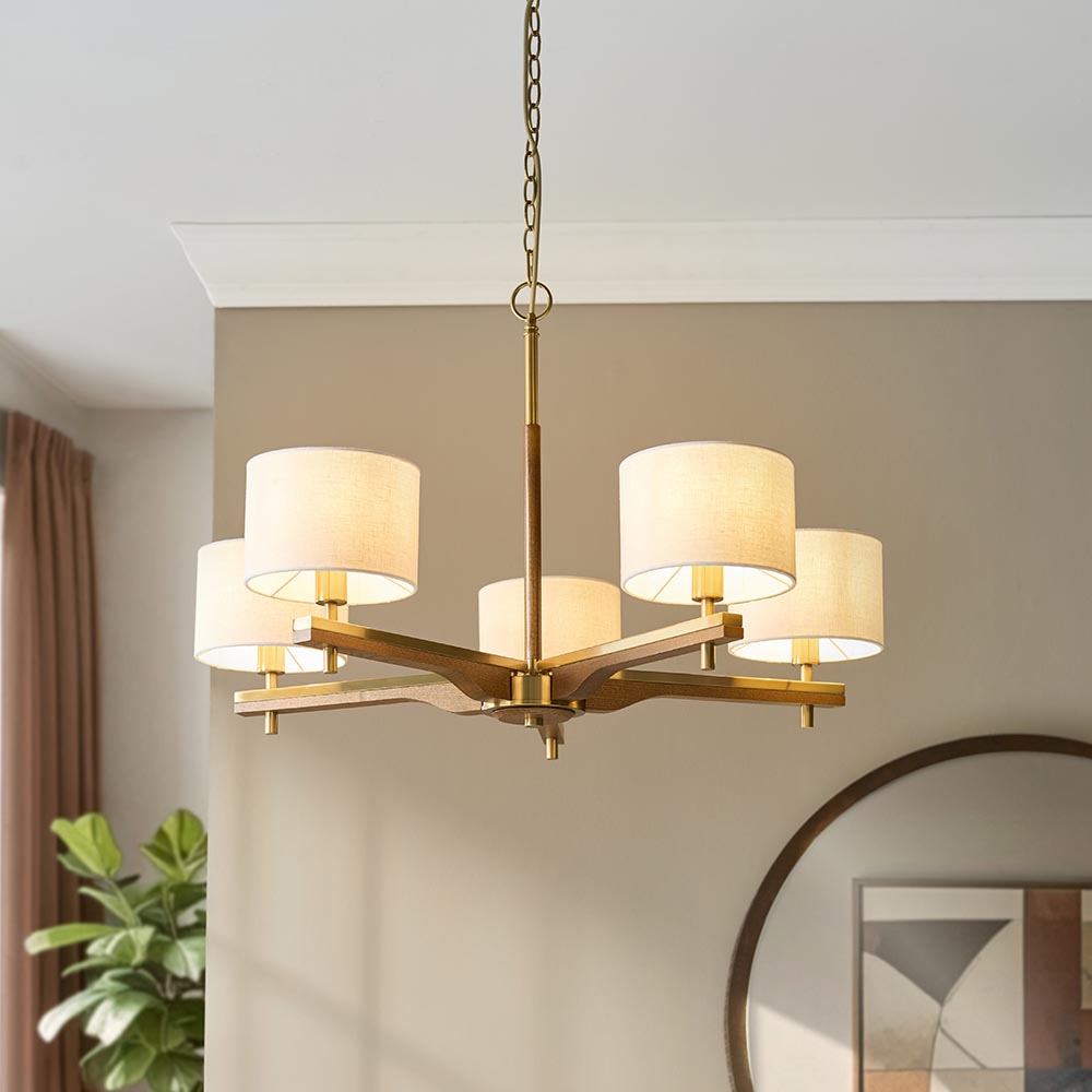 Bramwell 5 Light Pendant in brass and natural, with wood arms and fabric cylinder shades on a chain drop, shown above a dining table setting.