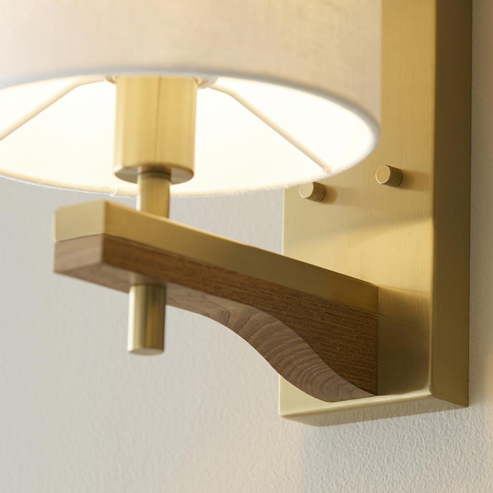Close-up of Endon Bramwell Wall Light in antique brass, showing the brushed brass bracket, oak-stained ash wood detail, and natural faux-linen shade.