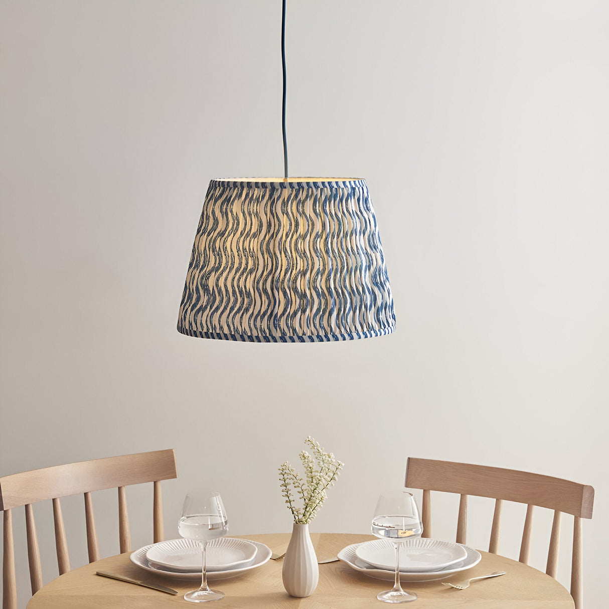 Brackmont Ripple Pendant in blue, a single-light fixture with a tapered fabric shade above a dining table with wooden chairs and place settings.