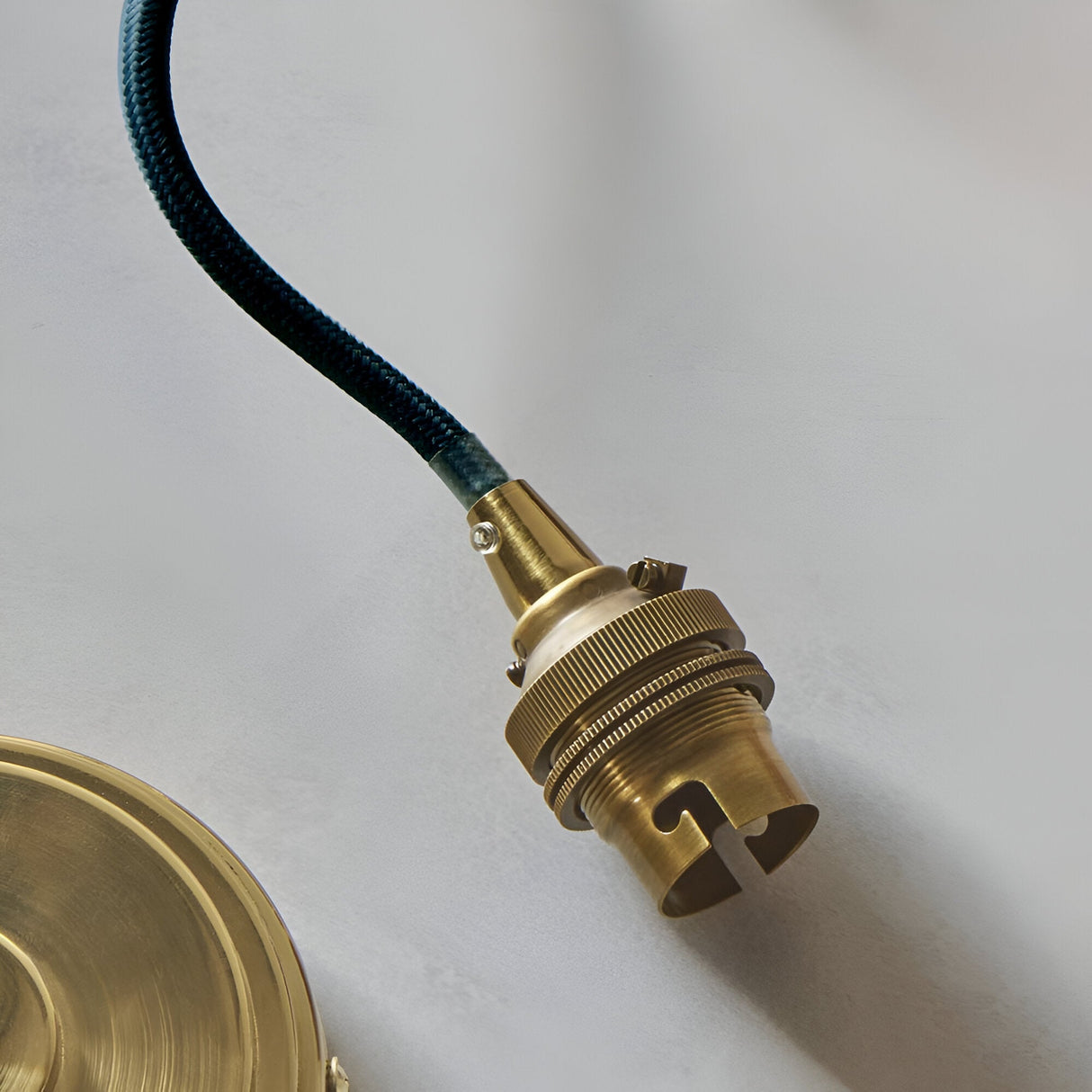 Close-up of the Brackmont Ripple Pendant's B22 lampholder in brushed antique brass, with blue fabric-braided cable, against a plain light background.
