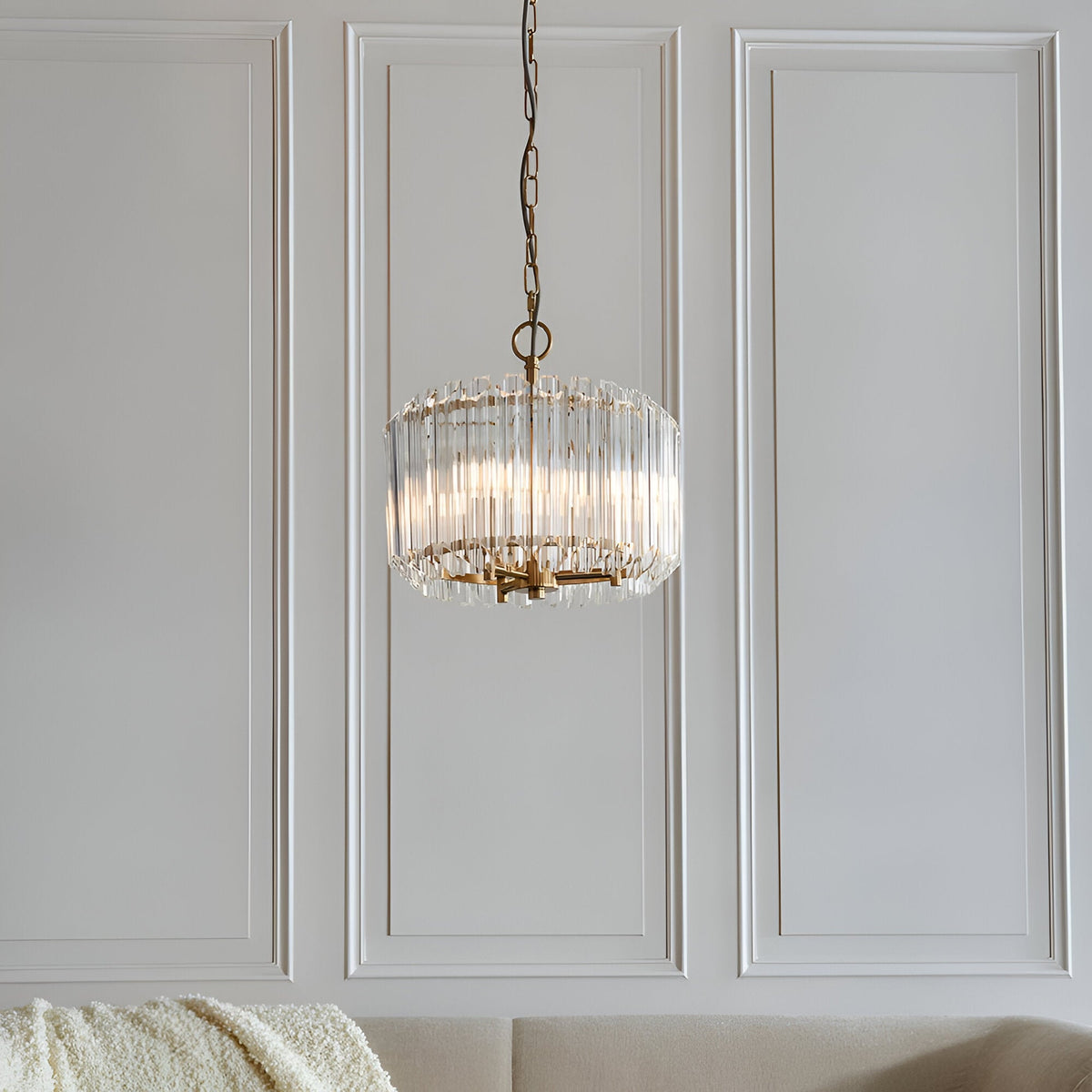 Endon Danebury 3 light pendant in brushed brass with tiered clear glass rods, suspended from a chain against a white panelled wall in a living room.