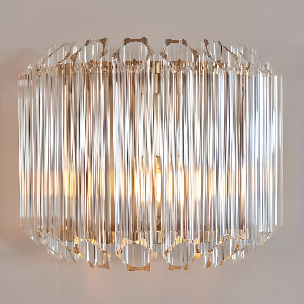 Endon Danebury wall light with faceted clear glass rods on a brushed aged brass frame, illuminated against a pale wall.