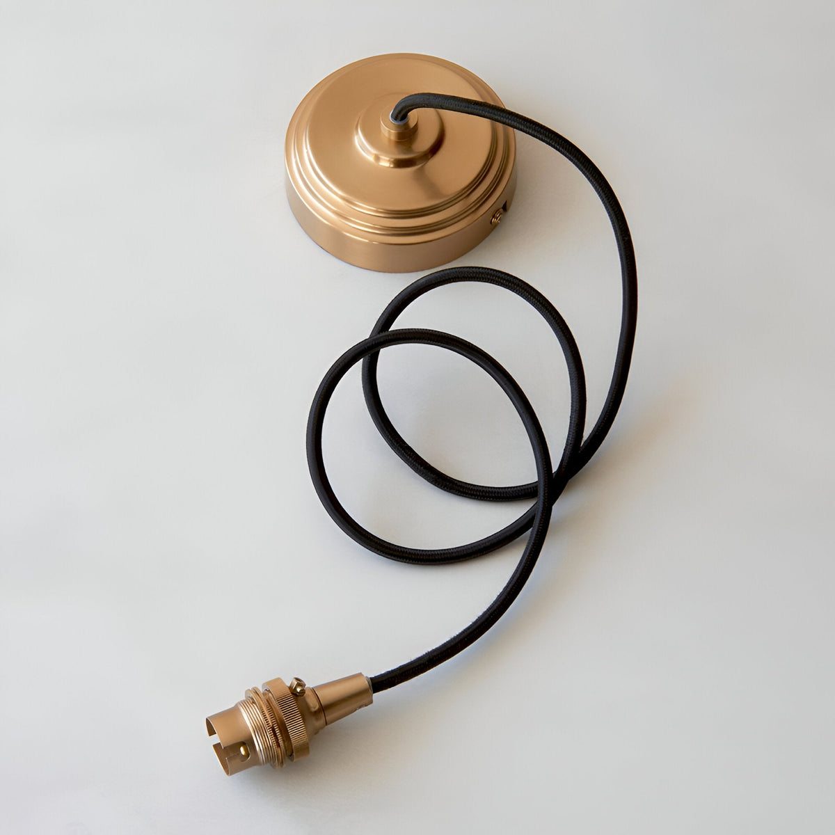 Endon Brackmont flex set with brushed aged brass ceiling rose, B22 lampholder and coiled black braided fabric cable on a plain background.