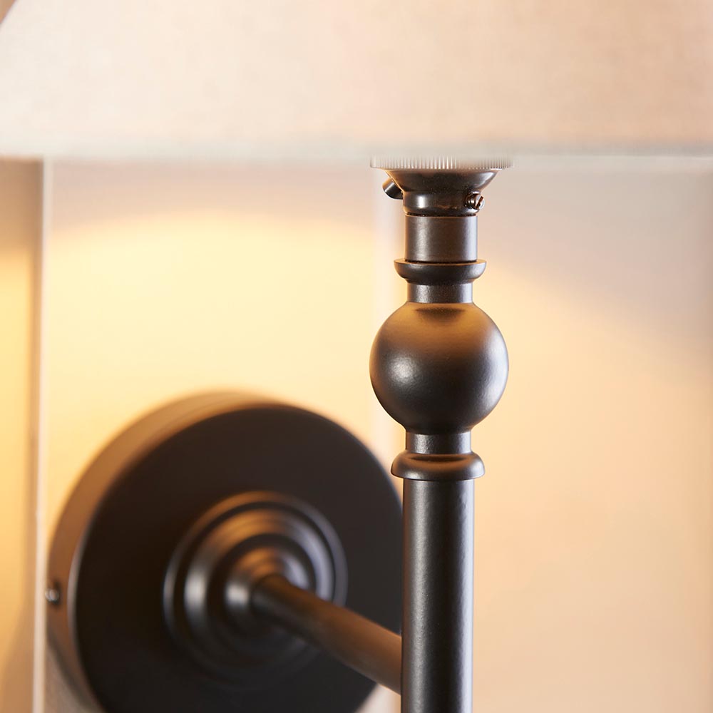 Close-up of the Endon Caldmere wall light in matt black, showing the spherical stem detail, round backplate, and tapered natural linen shade.