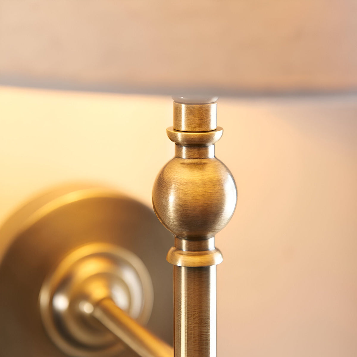 Close-up of the Endon Caldmere wall light showing the antique brass ball detail, upright stem and base of the natural linen shade.