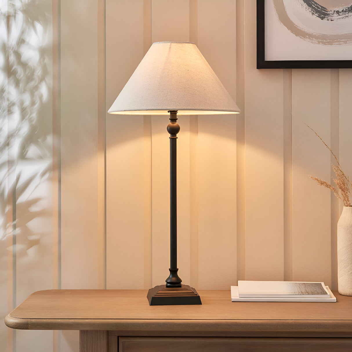 Endon Caldmont table lamp with slim turned matt black metal column and tapered natural linen shade, styled on a wood console beside framed art.