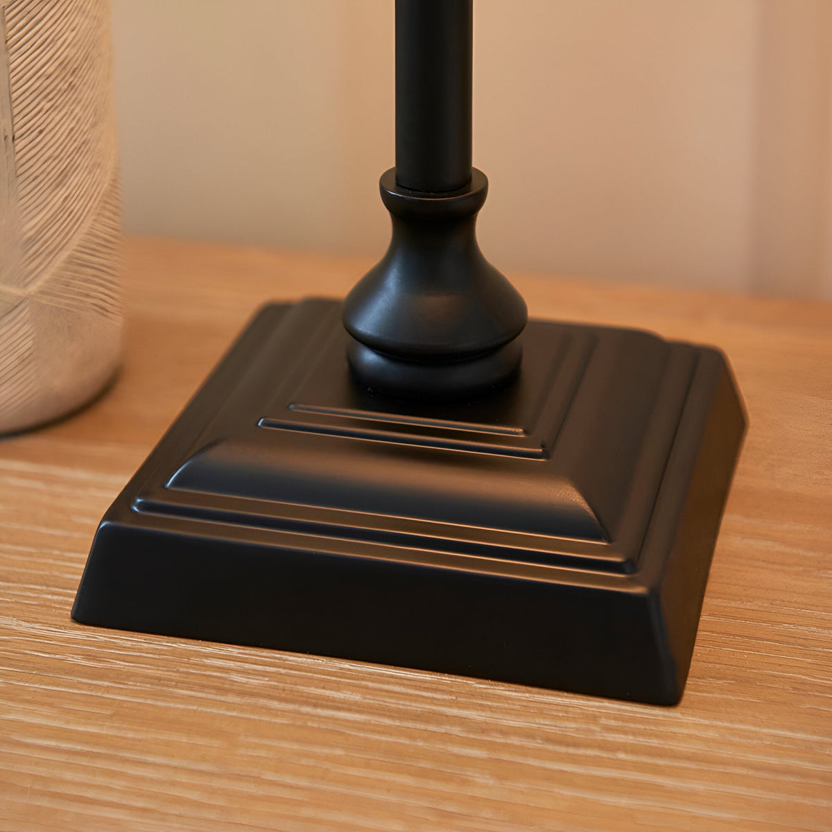 Close-up of the Endon Caldmont table lamp's matt black tiered square base and turned metal column on a wooden surface.