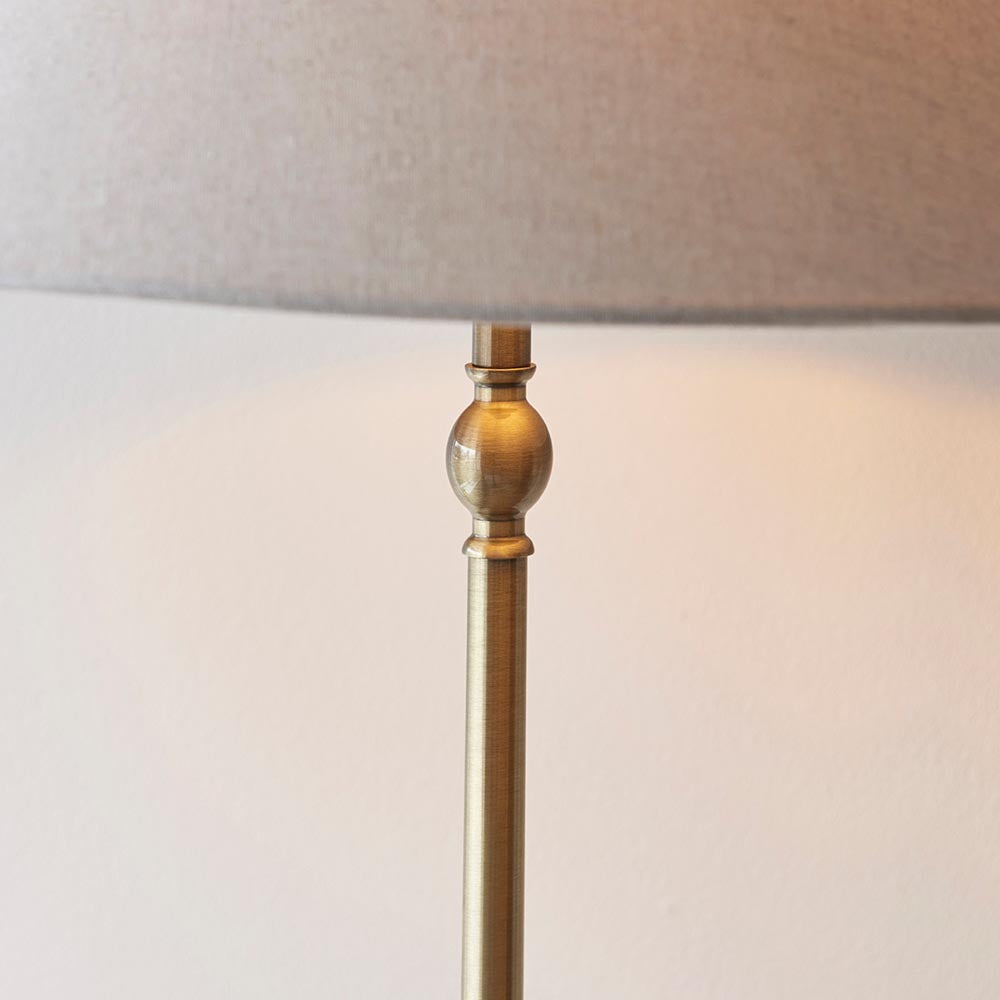 Close-up of the Endon Caldmere floor lamp's antique brass stem with decorative ball detail beneath a natural linen tapered shade.