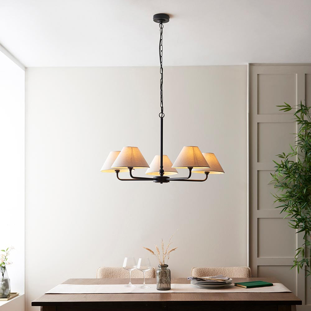 Endon Caldmere 5 Light Large Pendant in black with five tapered natural linen shades on a chain suspension, above a wooden dining table.