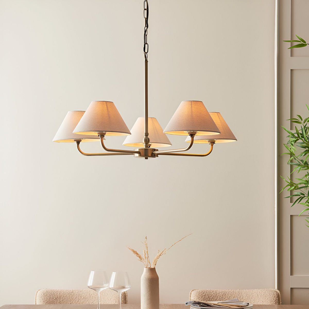 Caldmere 5 Light Large Pendant in brass with five tapered natural linen shades, hung above a dining table in a neutral-toned room.