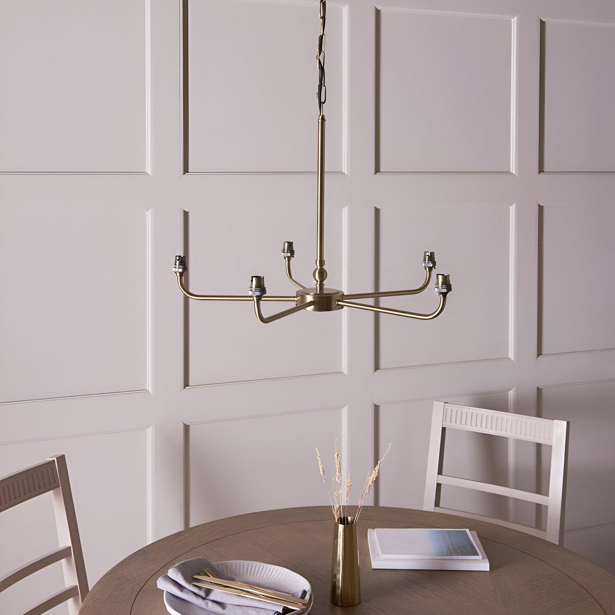 Caldmere 5 Light Large Pendant in brass, five curved arms radiating from a central rod, shown bare without shades in a dining room with panelled wall.