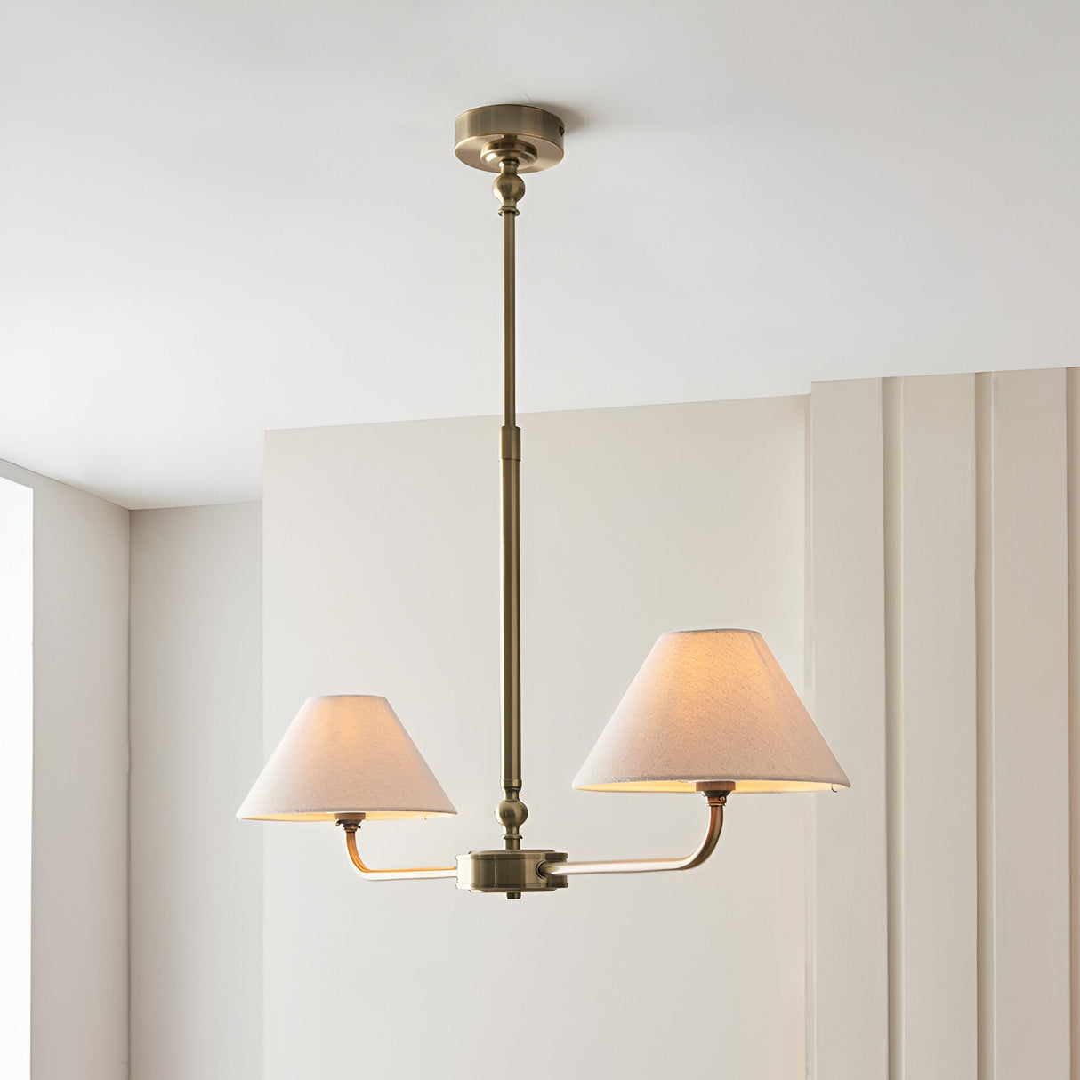 Caldmere 2-light pendant with brass stem and two tapered natural linen shades on a horizontal bar, shown hanging from a light ceiling in a room setting.