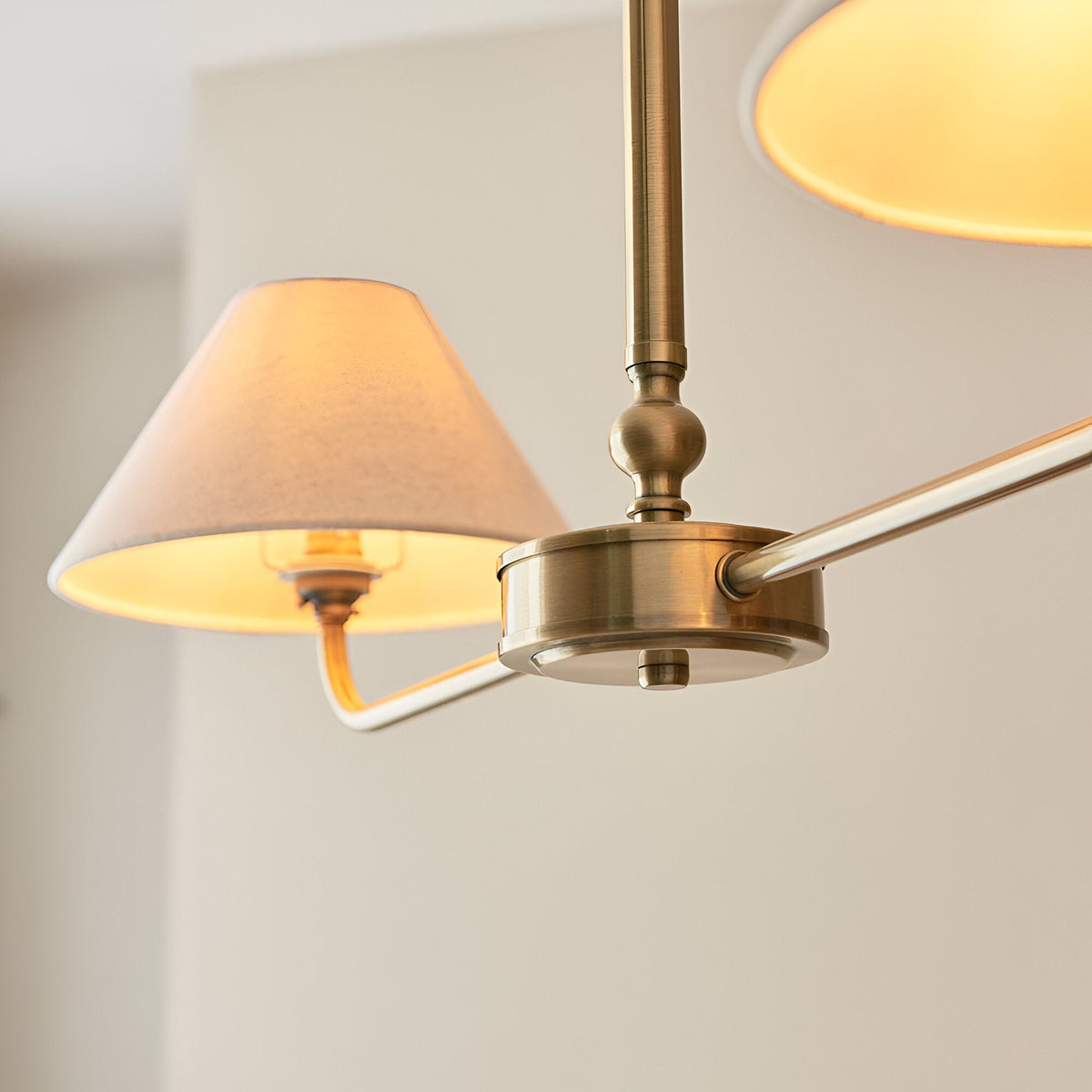 Close-up of the Caldmere 2 Light Pendant in brass, showing tapered natural linen shades on a swing arm with telescopic stem detail.