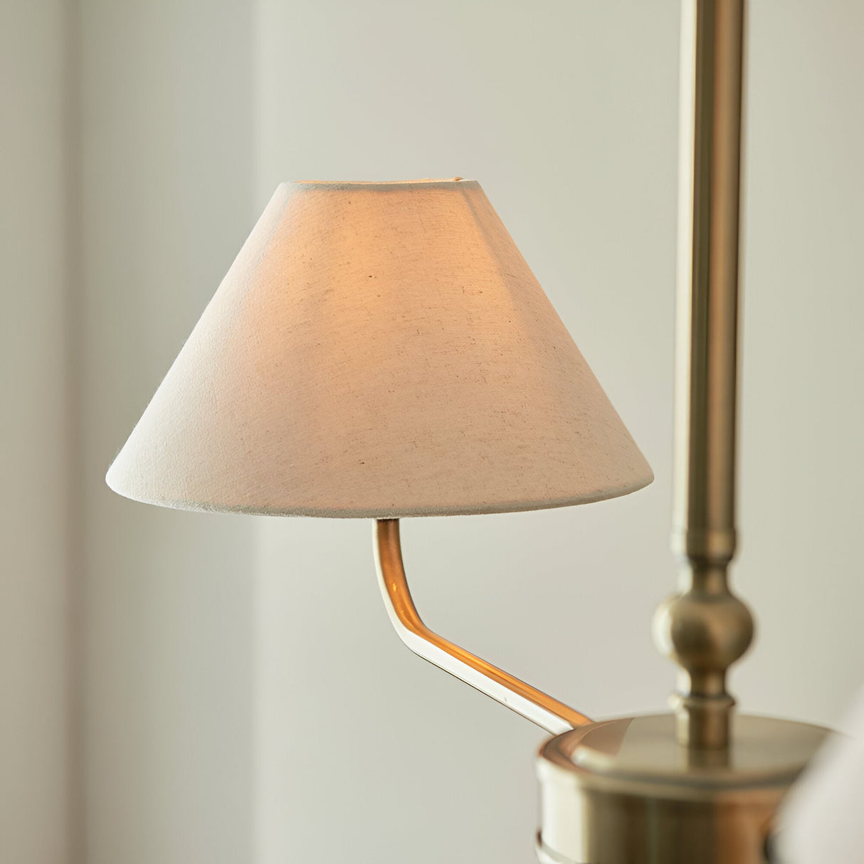 Caldmere pendant light close-up showing a tapered natural linen shade on a brass curved arm with visible brass stem, set against a plain light background.