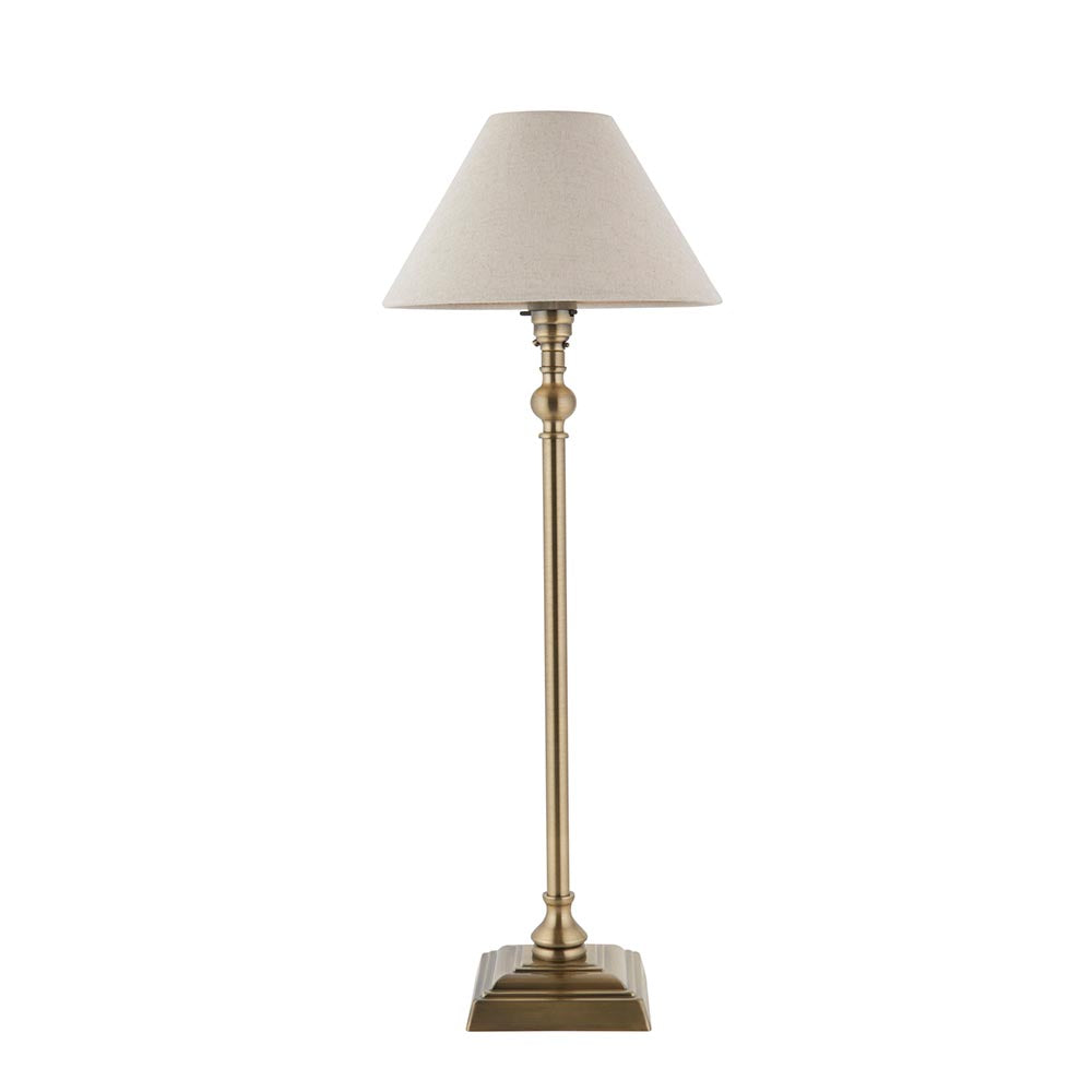 Endon Caldmont table lamp with a slim antique brass candlestick column, square stepped base and tapered natural linen shade, on a white background.