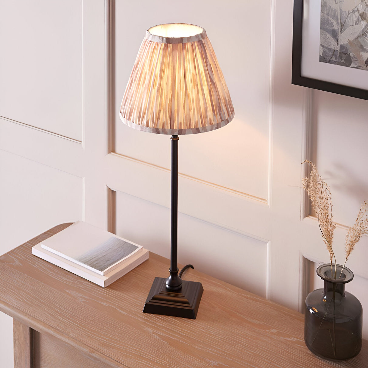 Caldmere Ikat Table Lamp in cream with pleated fabric shade on a matt black candlestick base, styled on a wooden console table.