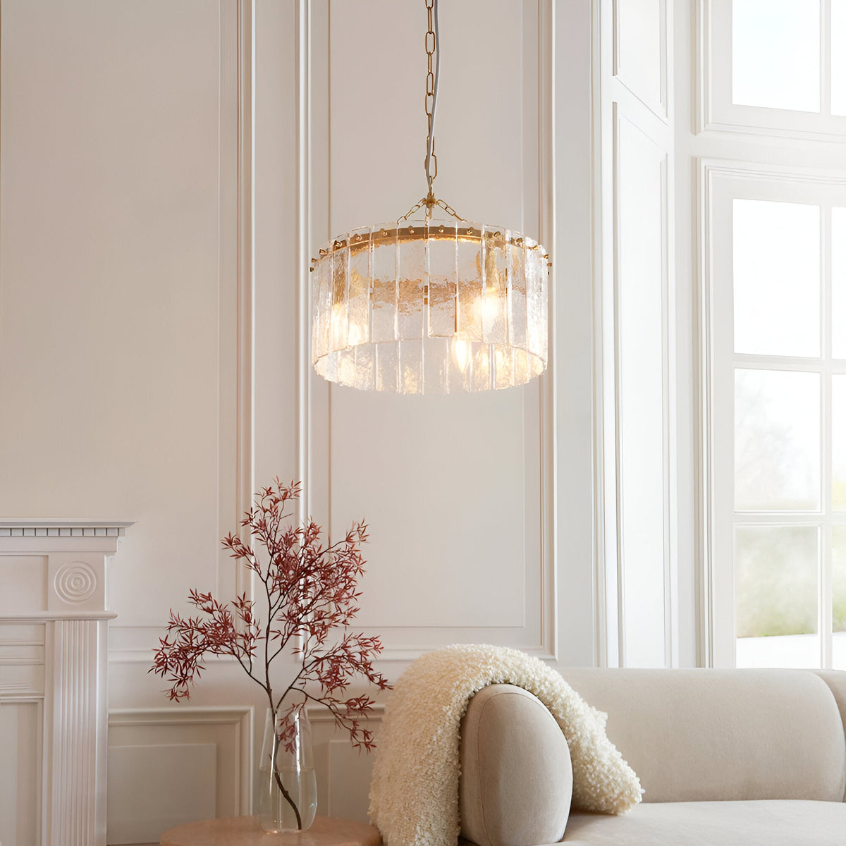 Brockhurst 3 Light Pendant in brass with textured clear glass panels, hung from a chain in a light-toned living room above a sofa.