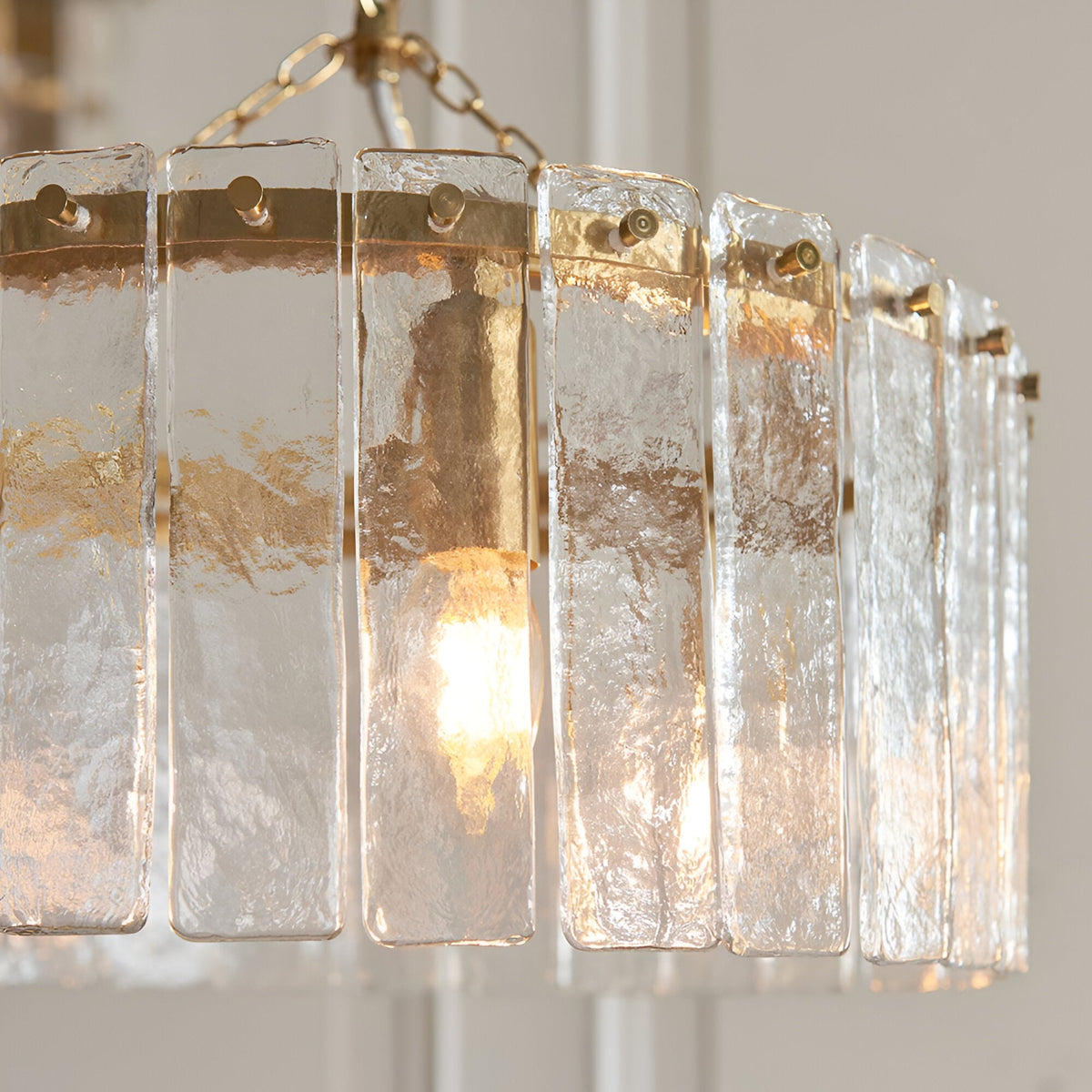Close-up of the Brockhurst 3 Light Pendant in brass, showing clear textured glass panels around a brass band with visible bulb and chain.