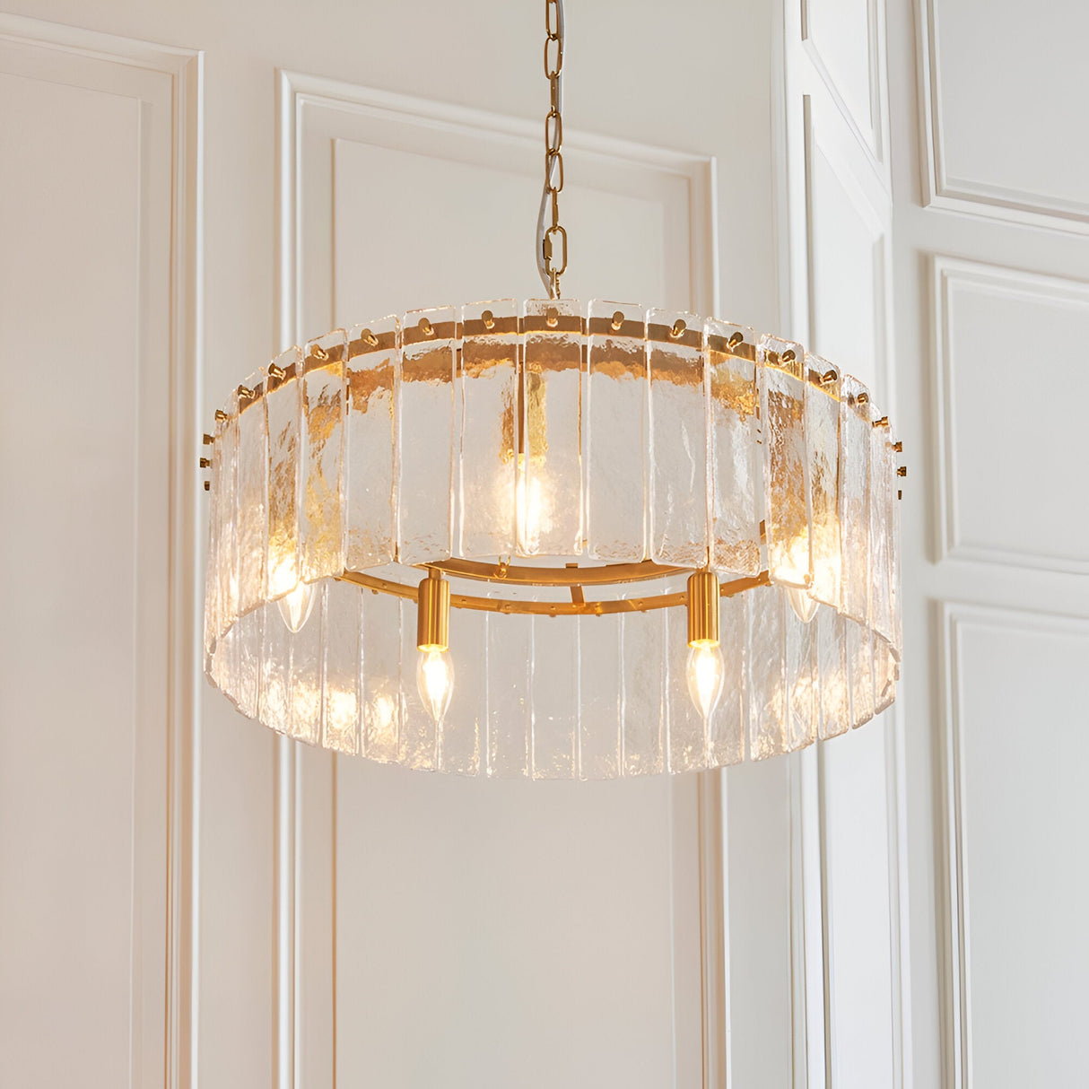 Endon Brockhurst 5 light pendant in brass with a ring of handmade textured glass panels on a chain, hung against panelled cream walls.