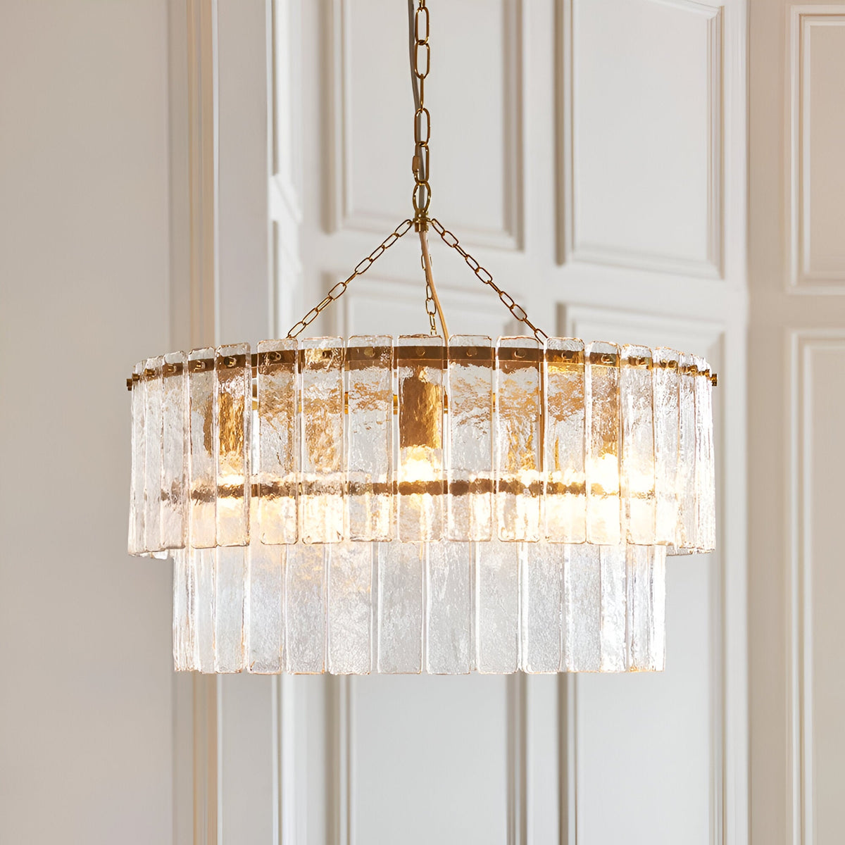 Endon Brockhurst 5 light chandelier in brushed aged brass with two tiers of textured glass panels, suspended from a chain against pale panelled doors.