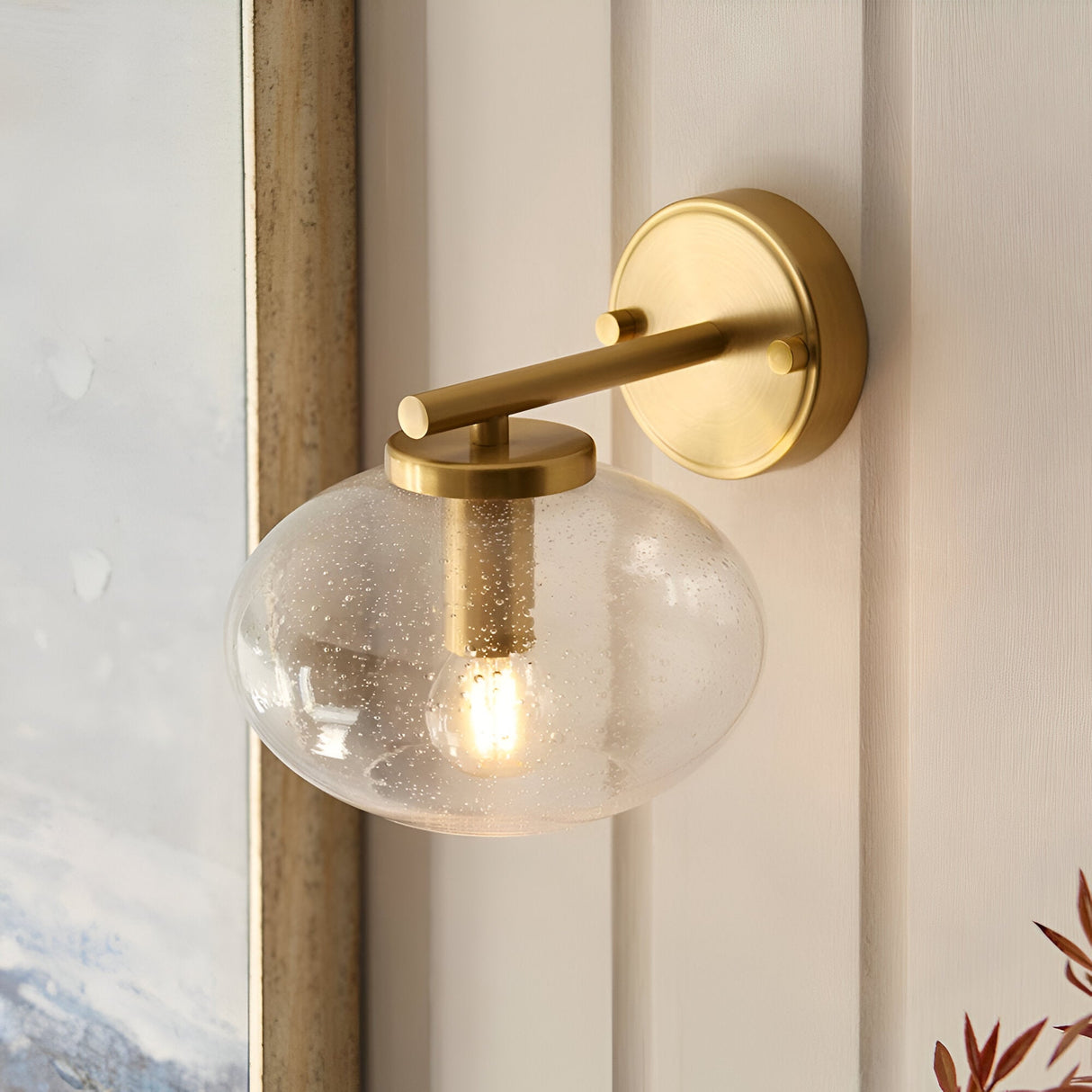 Endon Pemberton wall light in brass with a hand-blown clear bubbled glass oval shade, mounted beside a window in a light interior.