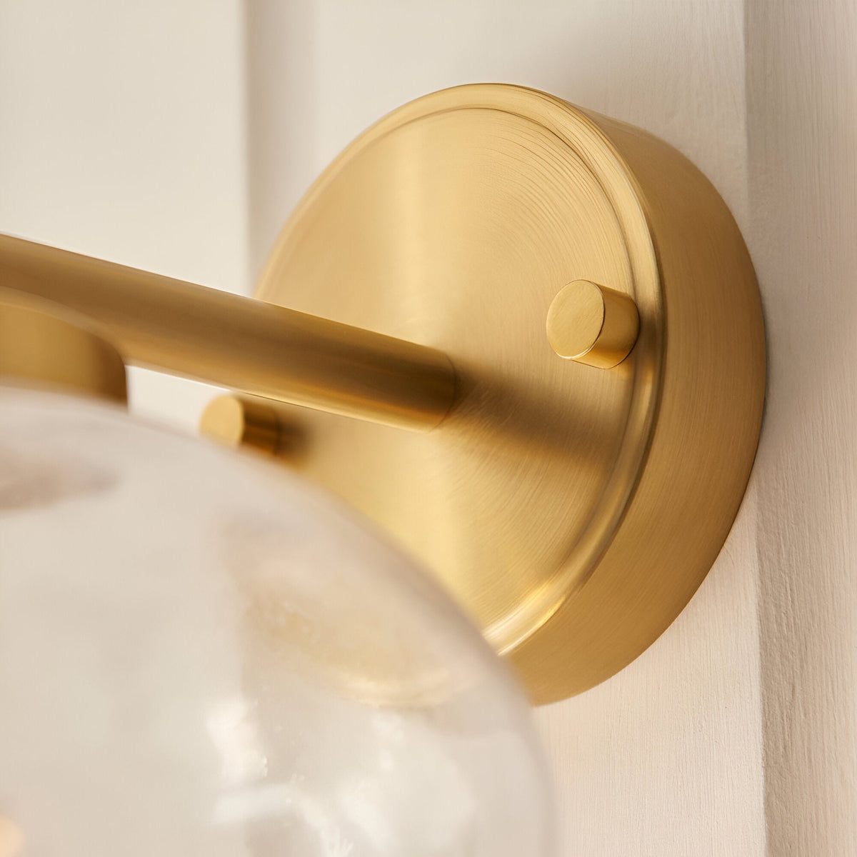 Close-up of the Endon Pemberton wall light's brass backplate and arm, showing the brushed finish and edge of the clear bubbled glass shade.