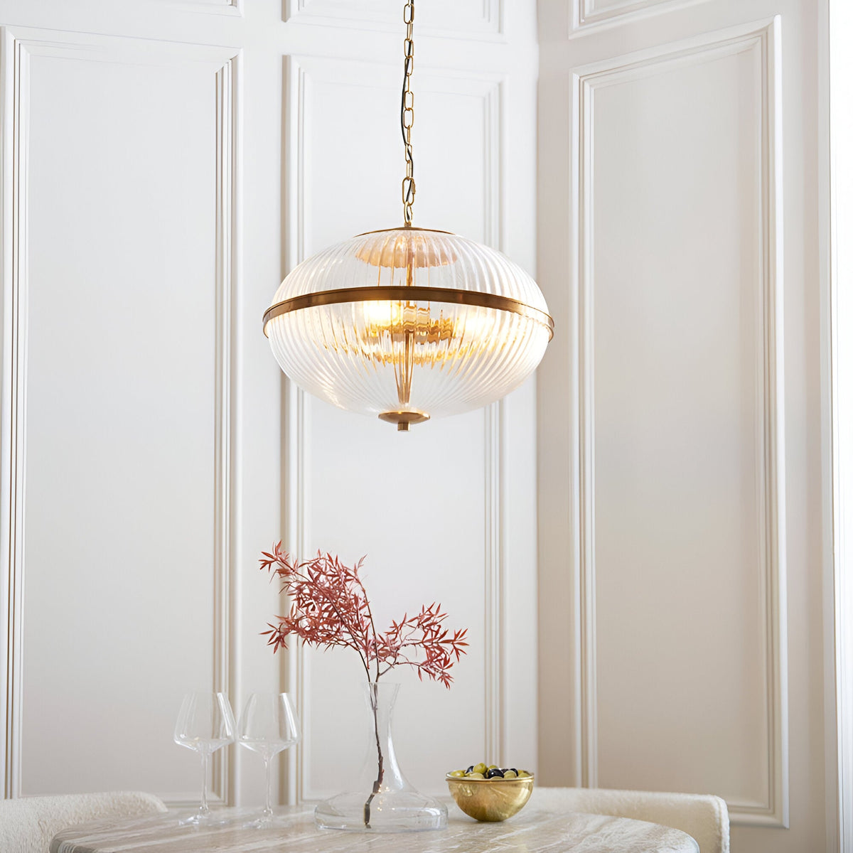 Langton 3 Light Pendant in brass with ribbed glass globe on chain, hanging in a panelled dining room above a table setting.