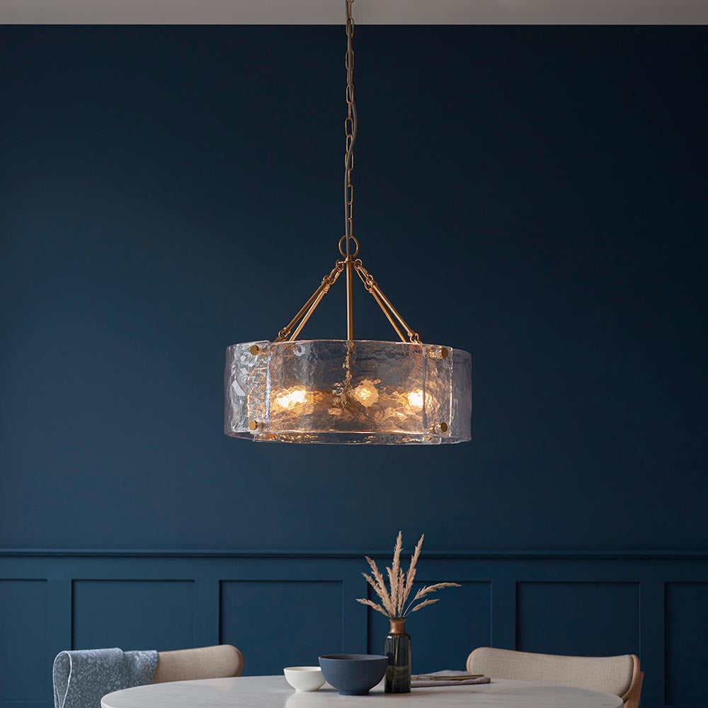 Endon Brockmont 6 Light Pendant in brass with rippled handmade glass cylinder shade, suspended by chain in a dining room with deep blue panelled walls.