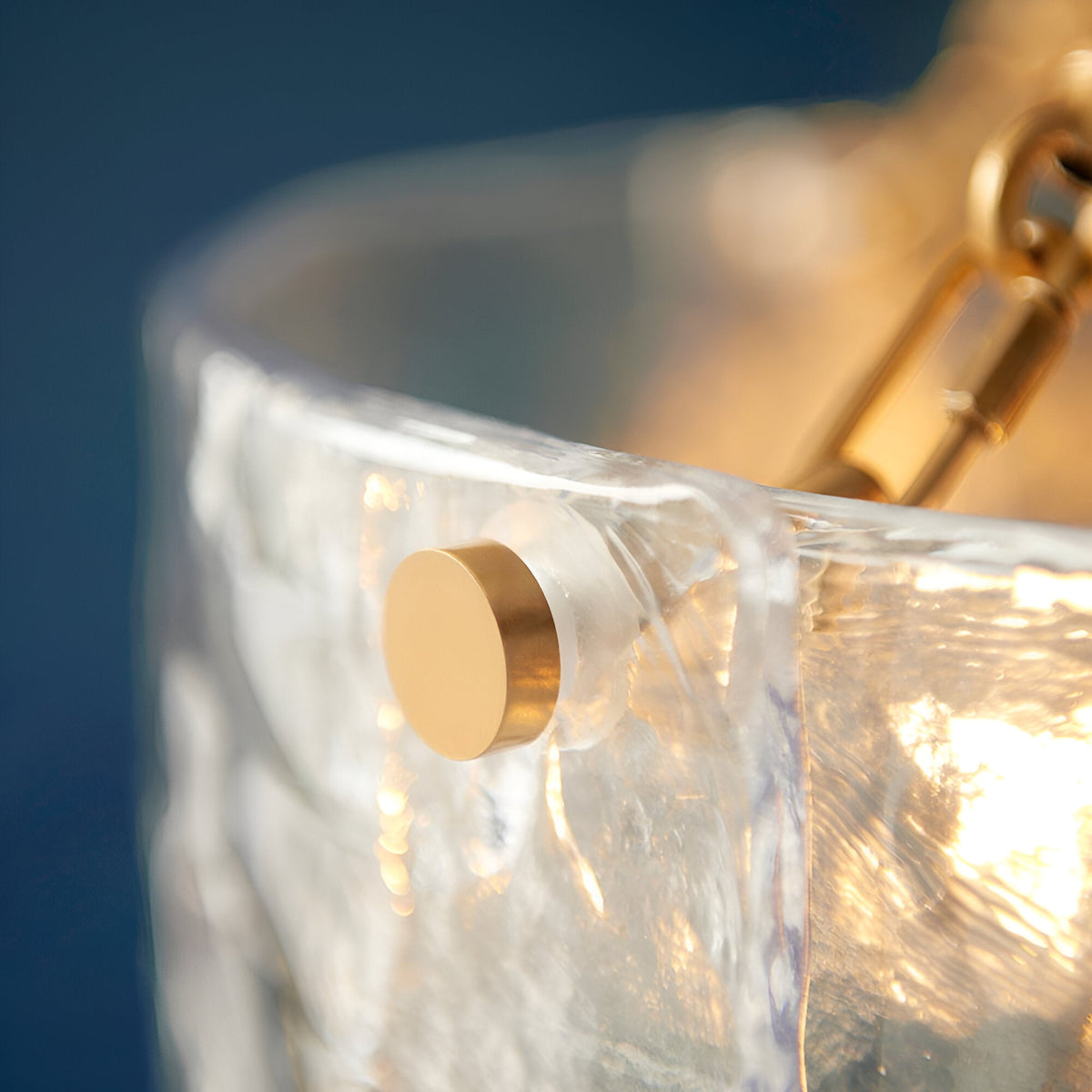 Close-up of the Endon Brockmont 6 Light Pendant showing a rippled handmade glass panel with a brushed brass fixing against a deep blue backdrop.