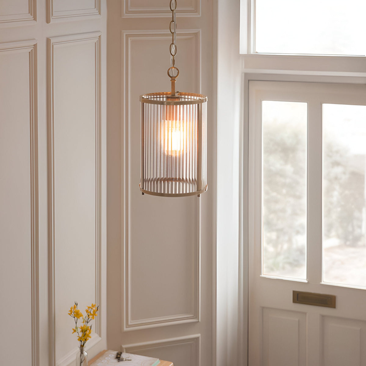 Endon Rothbury pendant light with ribbed clear glass cylindrical shade and antique brass frame, hung on a chain in a panelled hallway by a door.