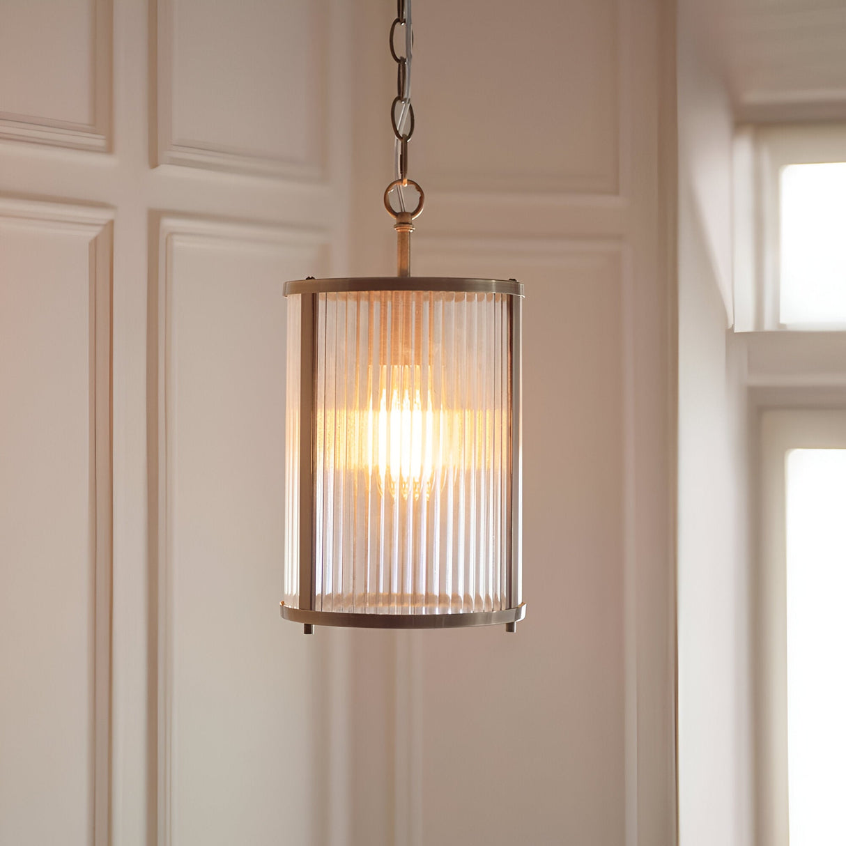 Endon Rothbury pendant with a ribbed clear glass cylindrical shade and antique brass frame, suspended from a chain in a panelled hallway.