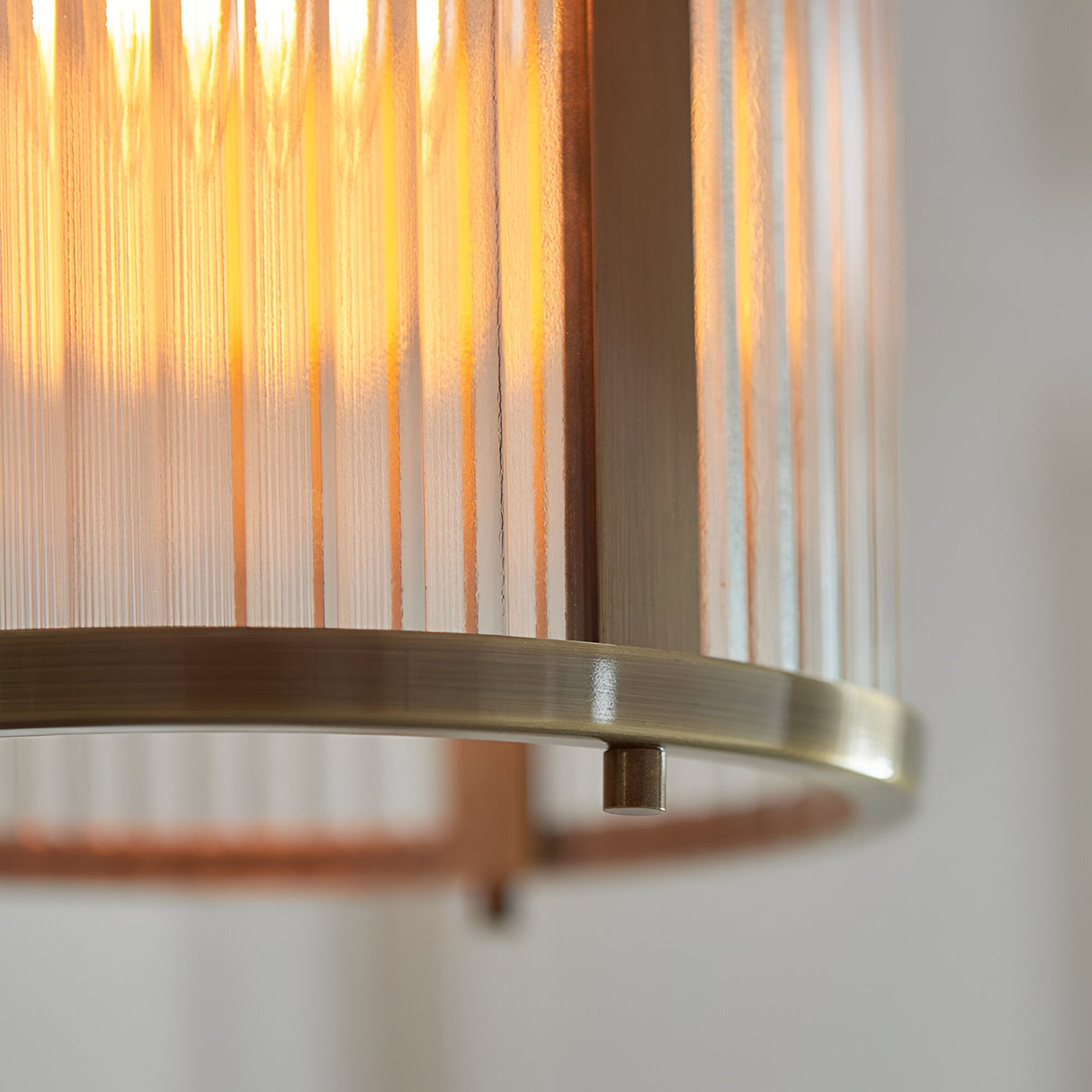 Close-up of the Endon Rothbury pendant showing the ribbed clear glass shade, antique brass base ring, and warm glow from the E27 filament lamp.