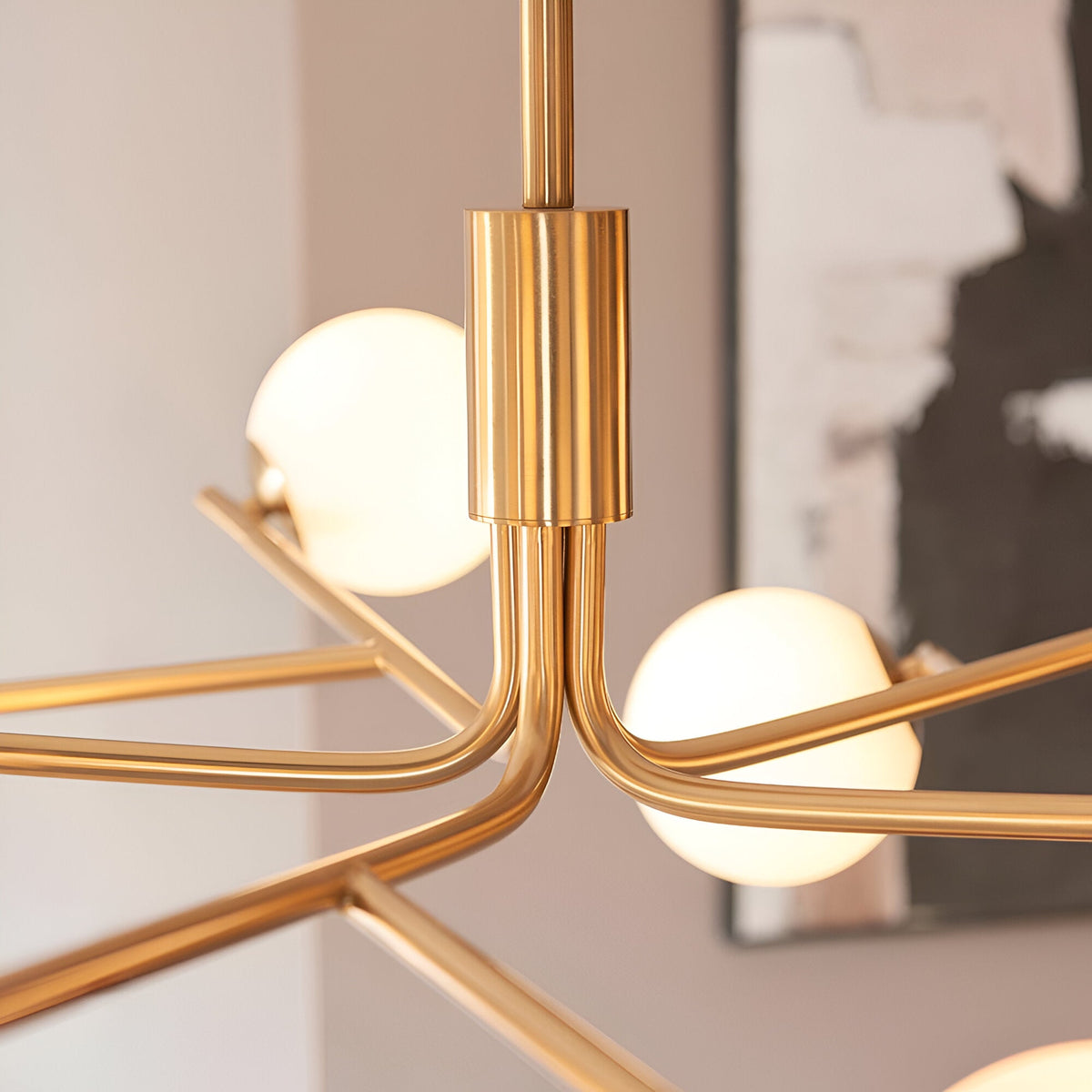 Close-up of the Grantham 10 Light Pendant in brushed aged brass, showing angled arms with matt opal glass spheres meeting at a telescopic central stem.