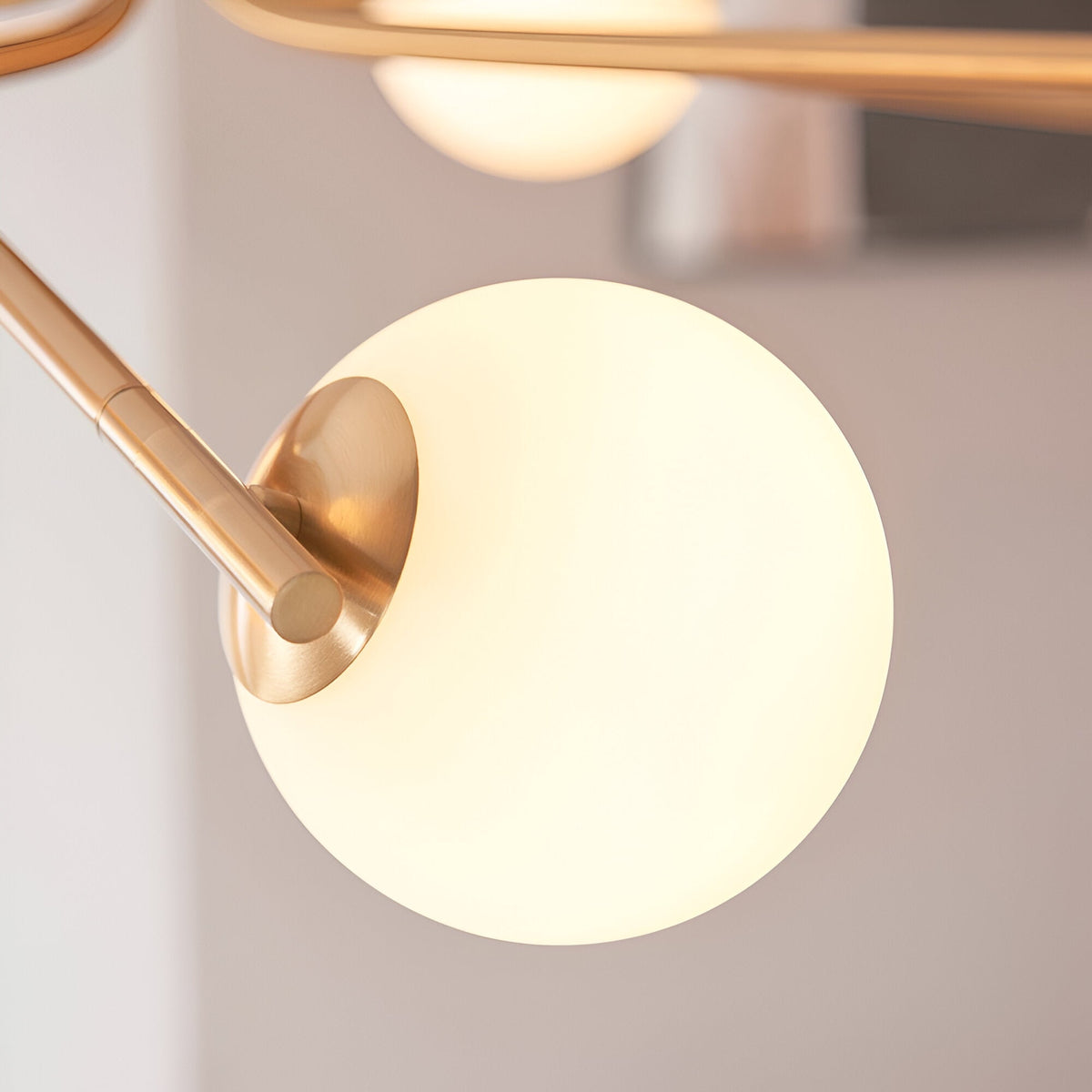 Close-up of the Grantham 10 Light Pendant in brushed aged brass, showing a matt opal glass globe on an adjustable arm against a light background.