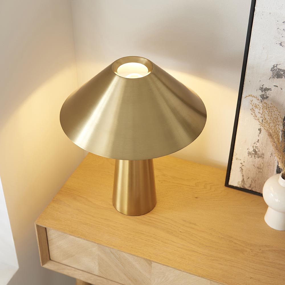 Endon Brockbourne table lamp in brushed antique brass with a wide conical shade and tapered base, styled on an oak console beside a framed print.