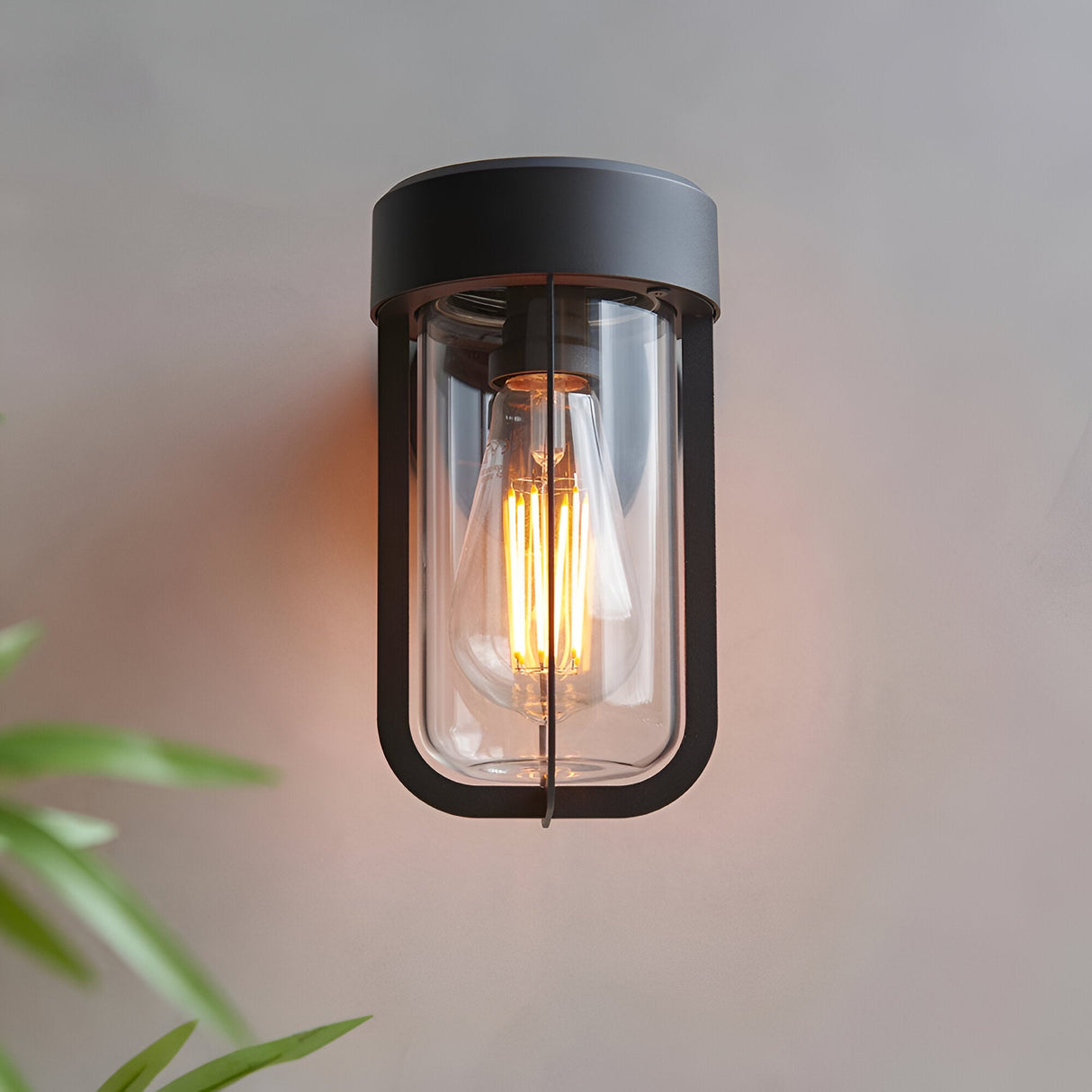 Caldwell Wall Light in matt black die-cast aluminium with clear glass shade and visible E27 bulb, industrial style, shown lit against a plain wall.