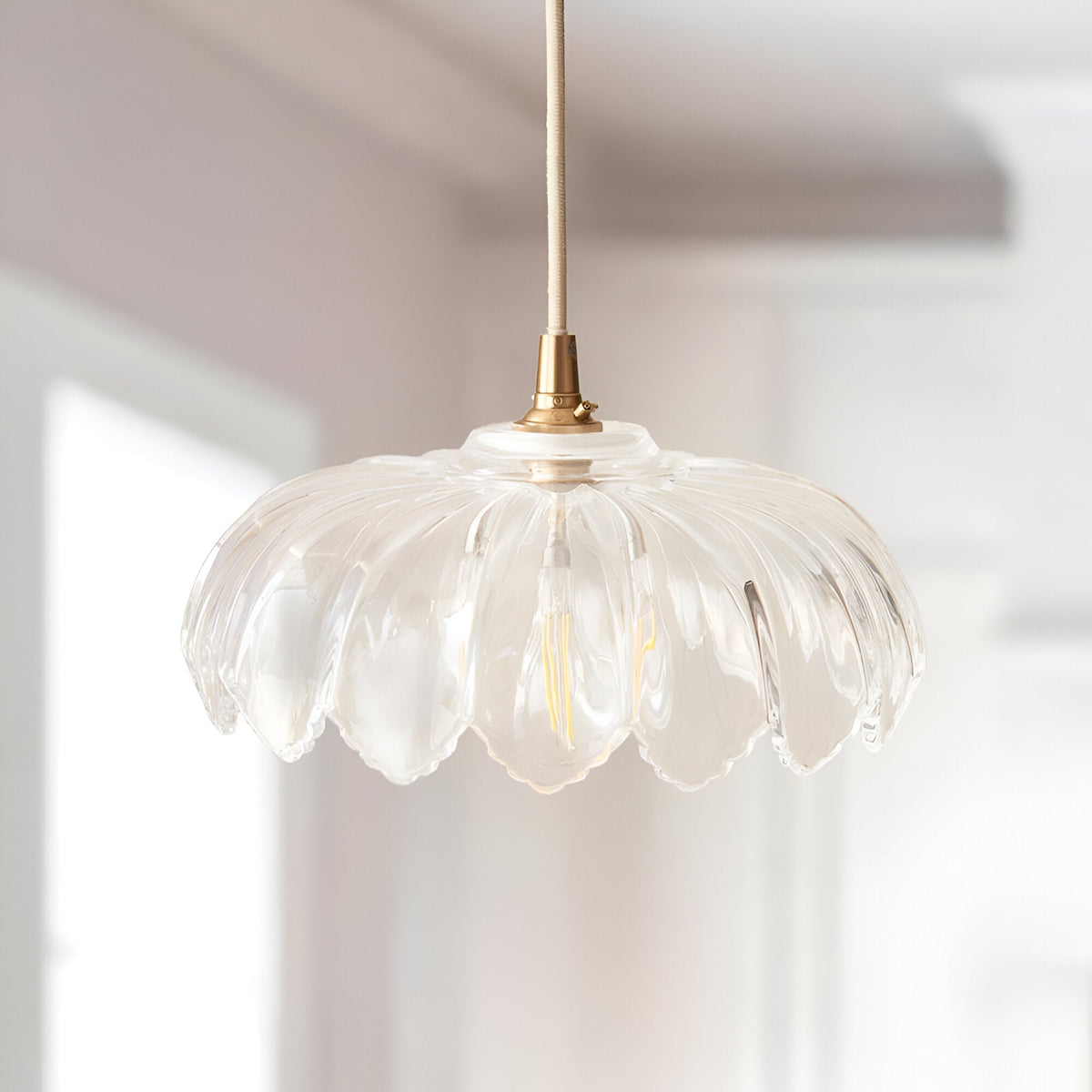 Ashwick clear glass pendant shade with scalloped edge and brass fitting, shown hanging in a bright kitchen setting.