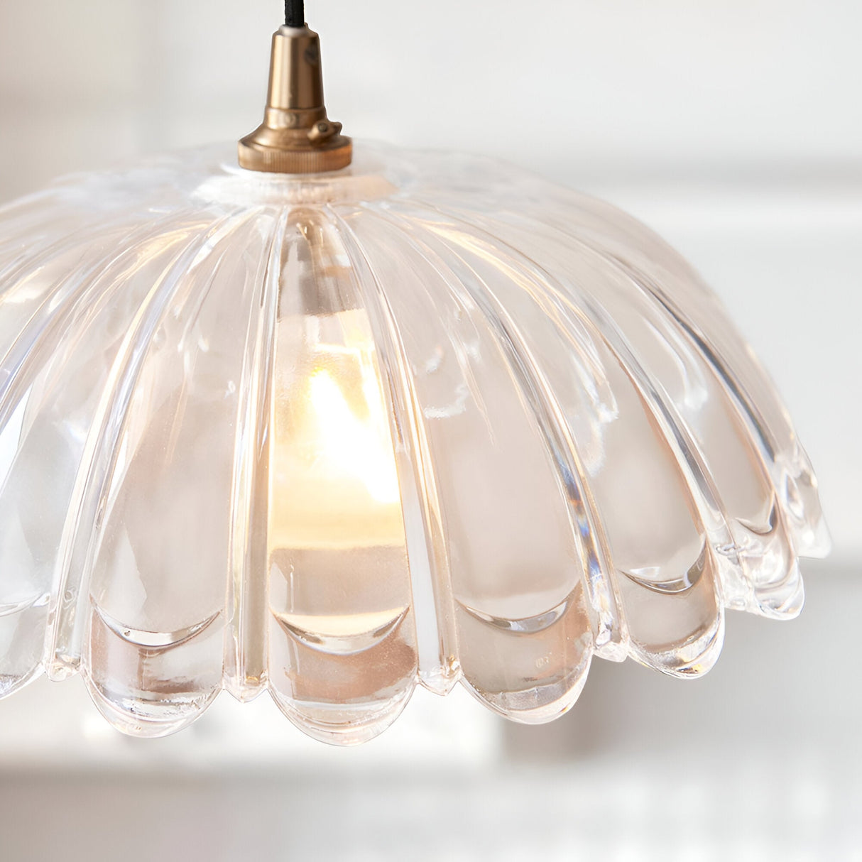 Endon Bevcombe scalloped clear glass domed pendant shade illuminated by a warm filament lamp, suspended from an antique brass fitting and braided black flex.