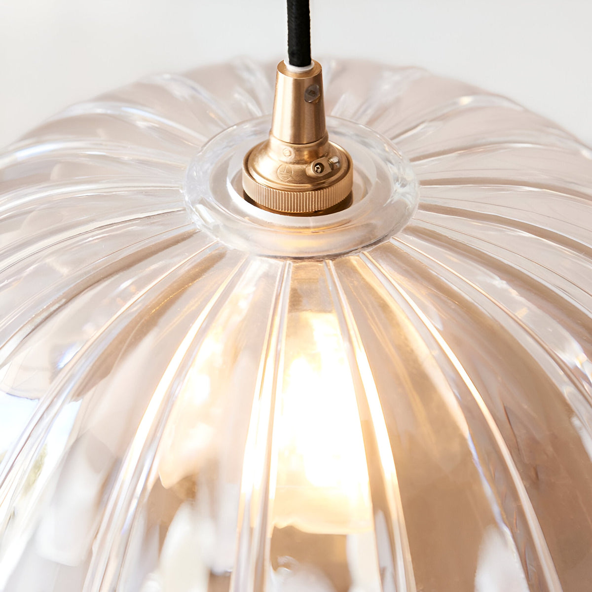Close-up of the Endon Bevcombe clear glass pendant shade showing its scalloped domed form and brass lamp holder with black braided flex.