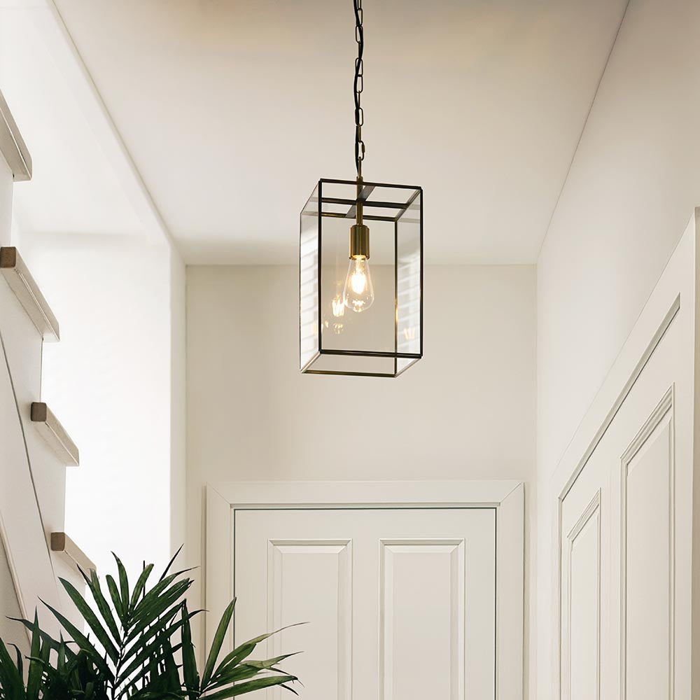 Endon Haddon Grand lantern pendant in brushed aged brass with clear glass panels and exposed E27 filament bulb, hung on a chain in a hallway.